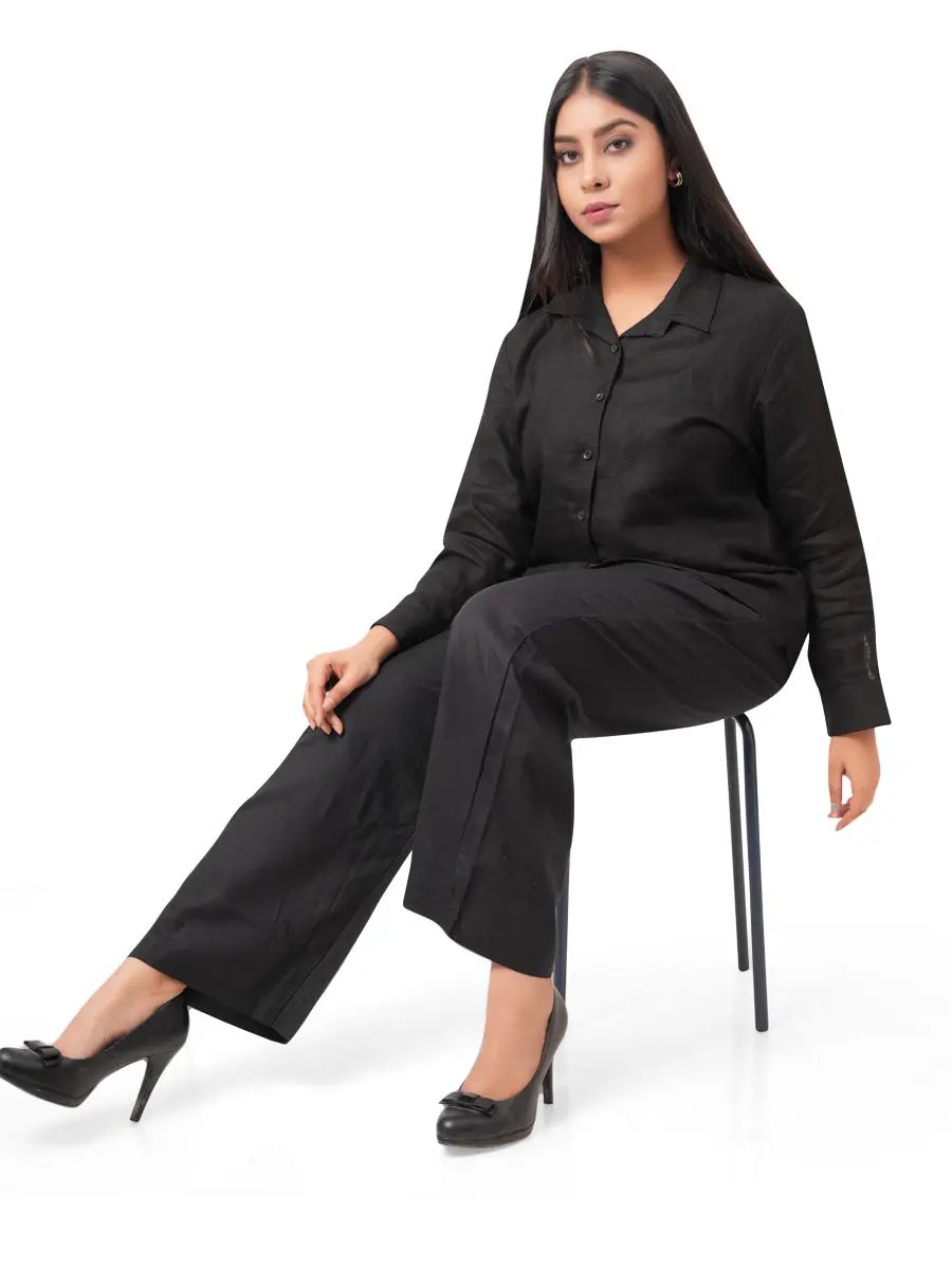 Woman wearing a black linen co-ord set sitting on a chair against a white background