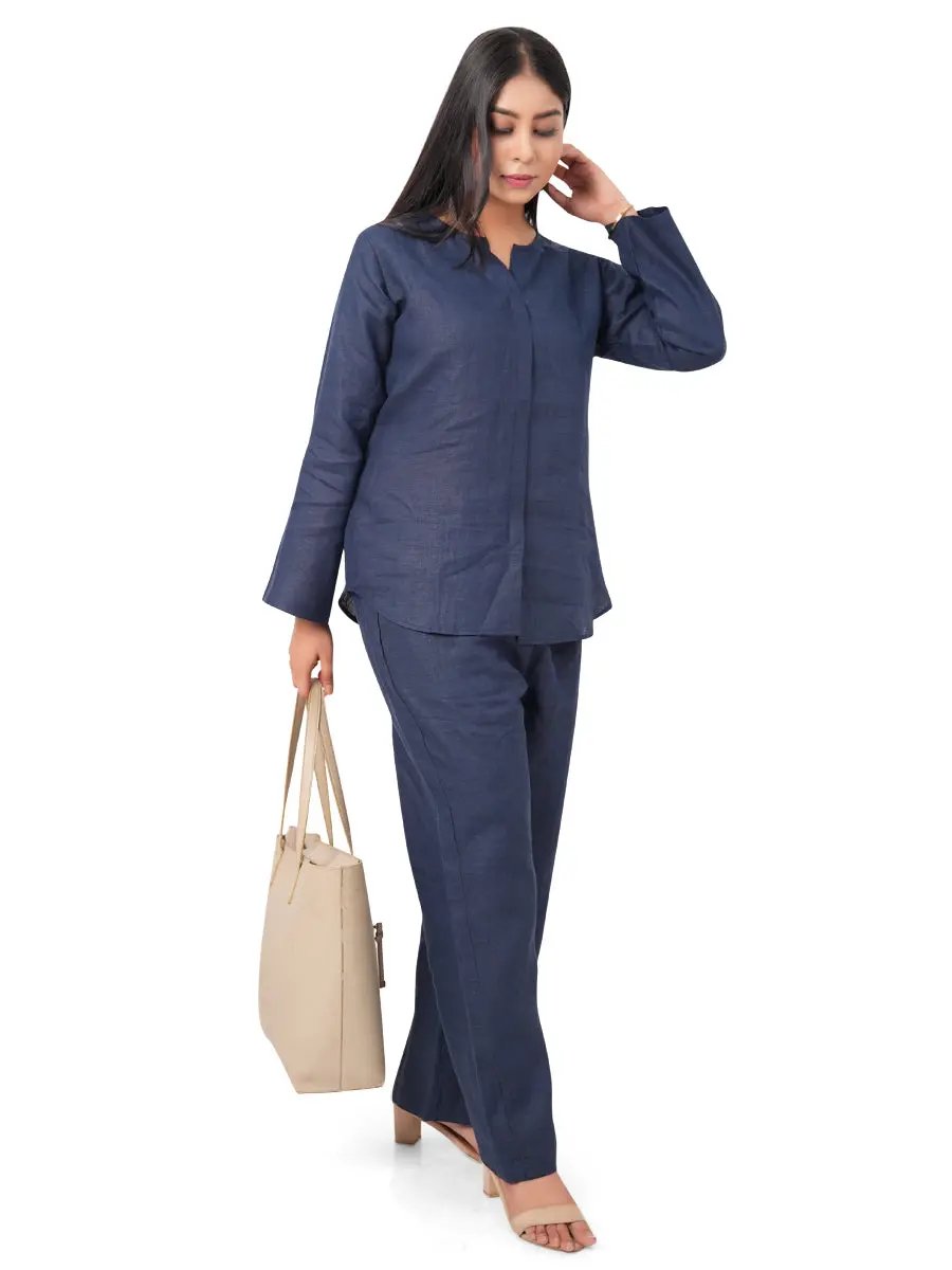 A woman in a navy blue pure linen co-ord set holding a beige handbag on a white background