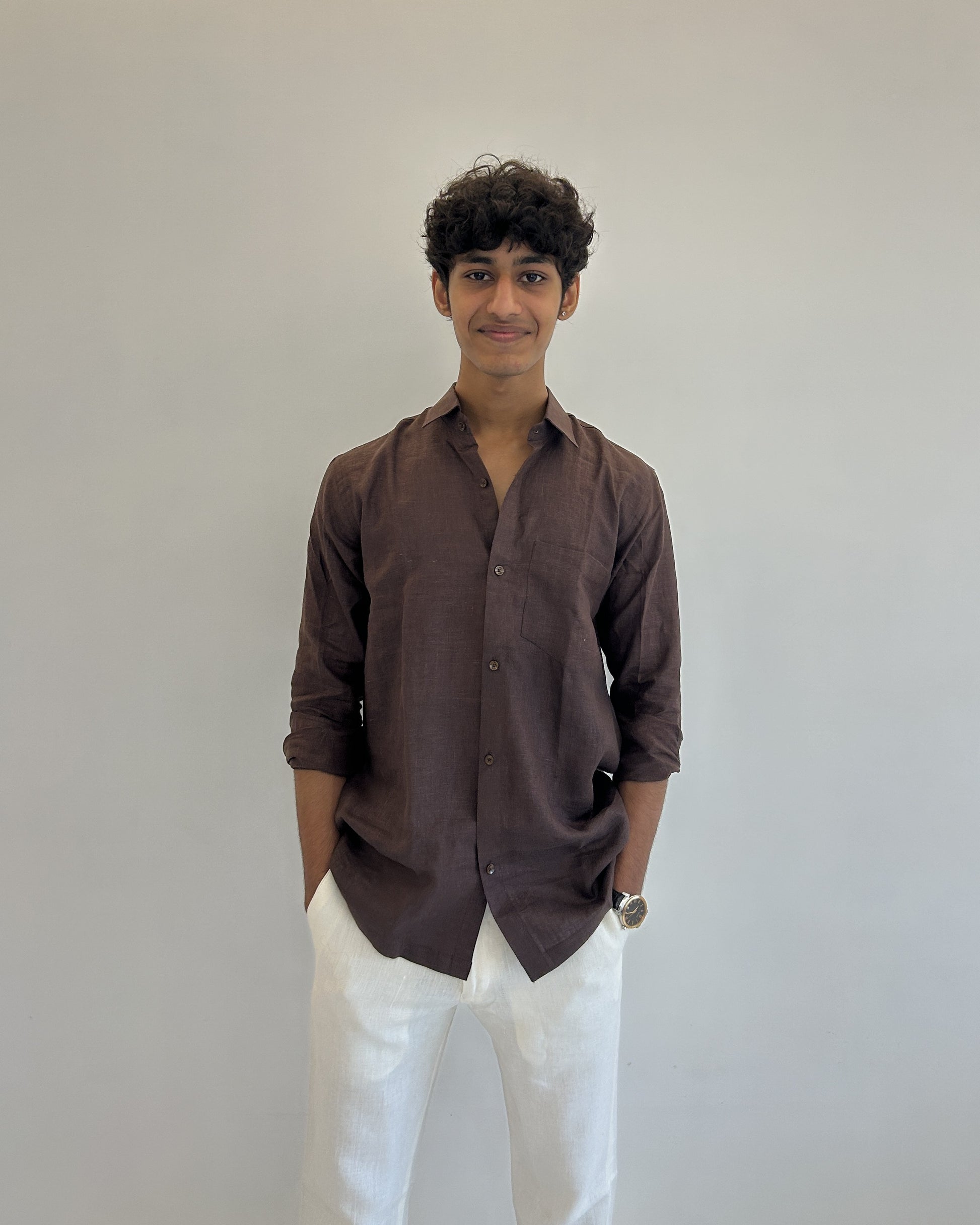 Person wearing a brown linen shirt and white pants against a plain background