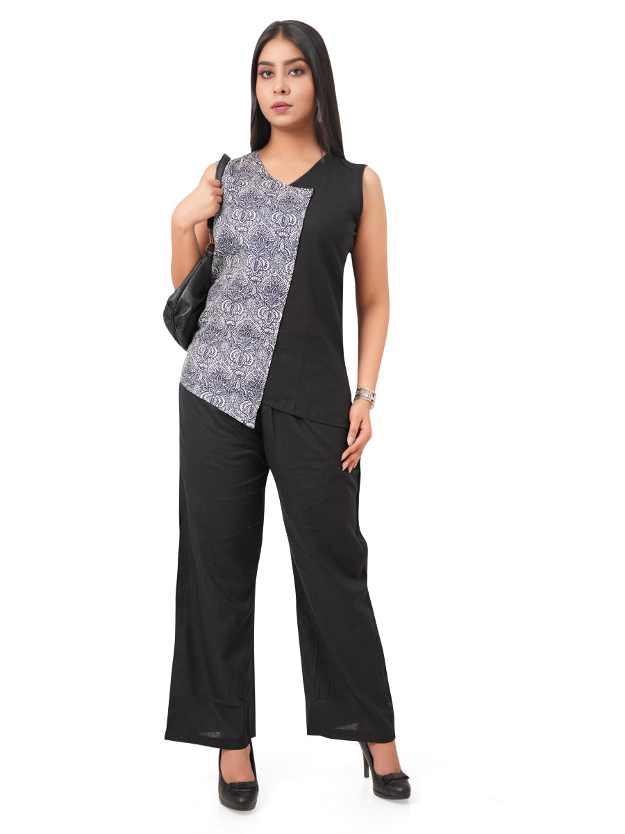 a woman wearing a black and patterned sleeveless linen top with wide-leg pants on a white background, carrying a bag
