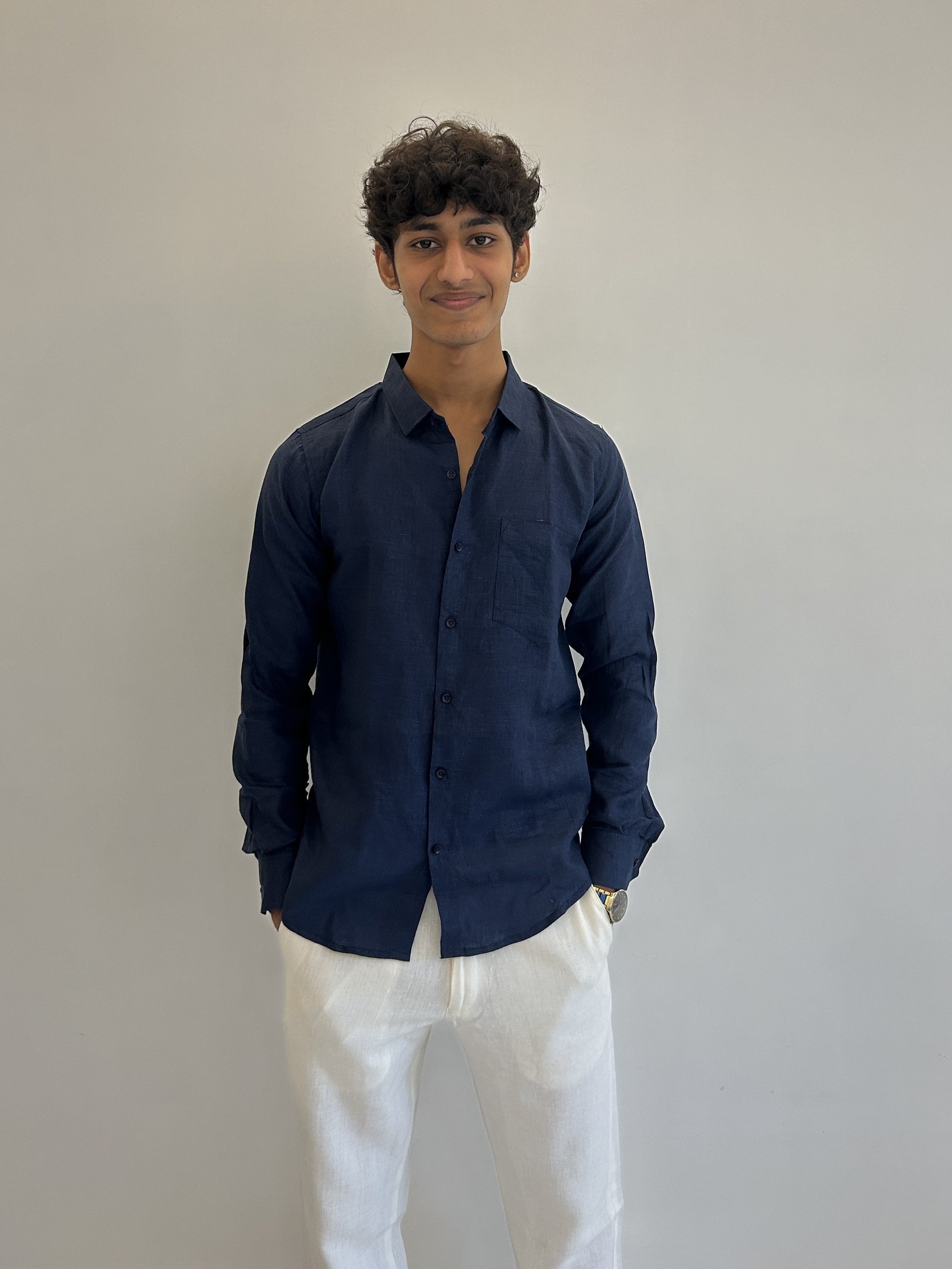Person wearing a navy blue linen shirt and white linen pants against a plain background
