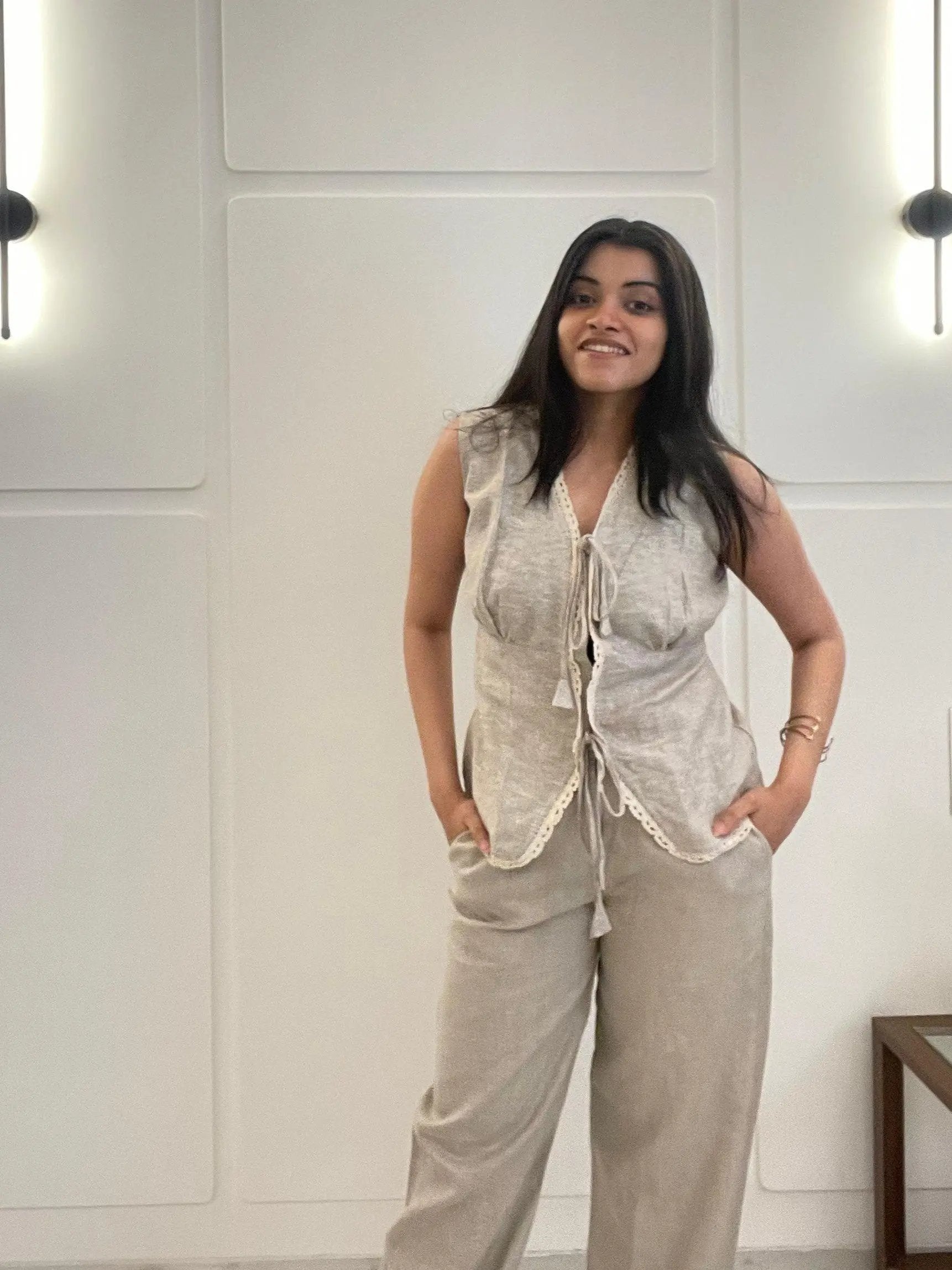 A woman wearing a beige linen waistcoat, sleeveless, and pants in a room with white walls.