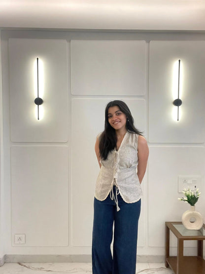 A woman wearing a beige linen waistcoat is standing in a modern interior setting with light-colored walls and minimal decor.