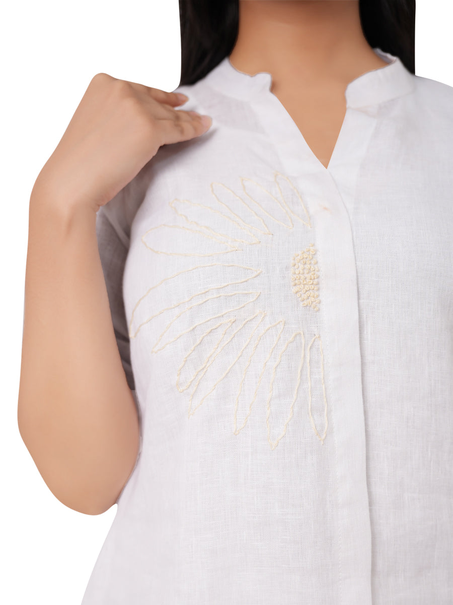 A white embroidered linen top worn by a person on a white background