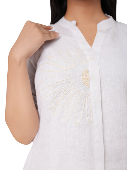 A white embroidered linen top worn by a person on a white background
