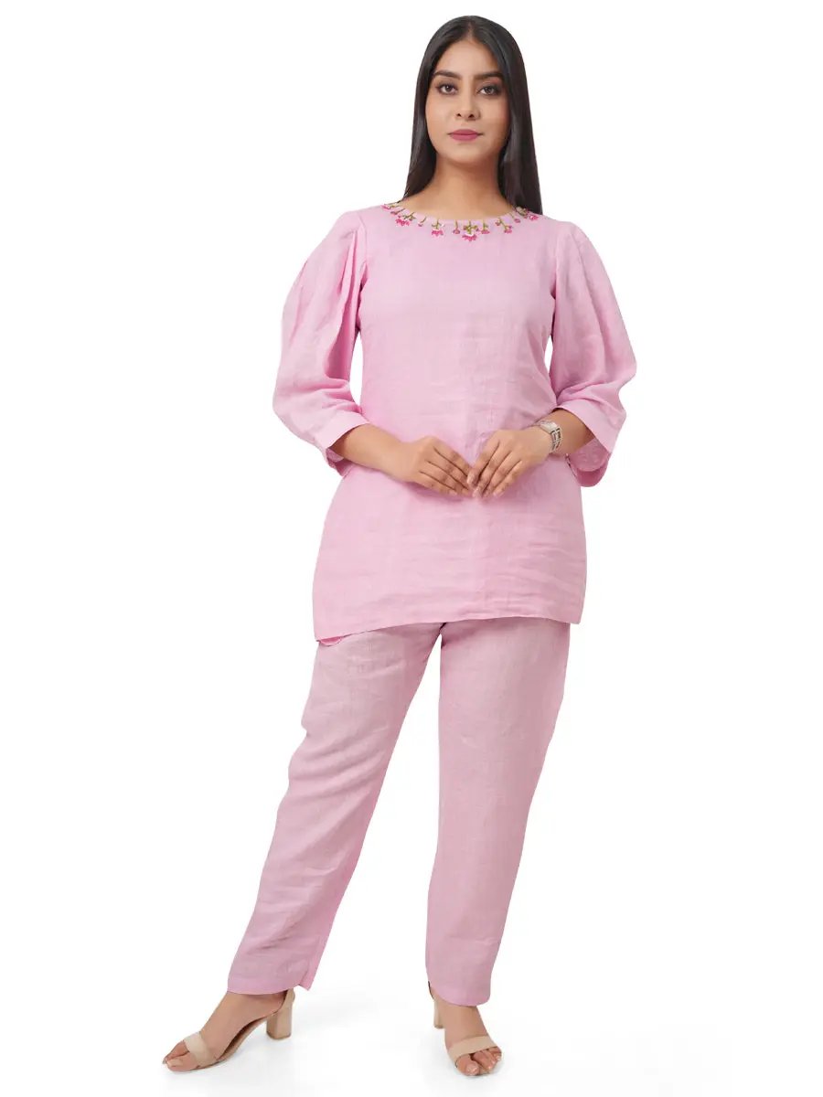 Woman wearing a pink pure linen co-ord set with floral embroidery on a white background with a front view