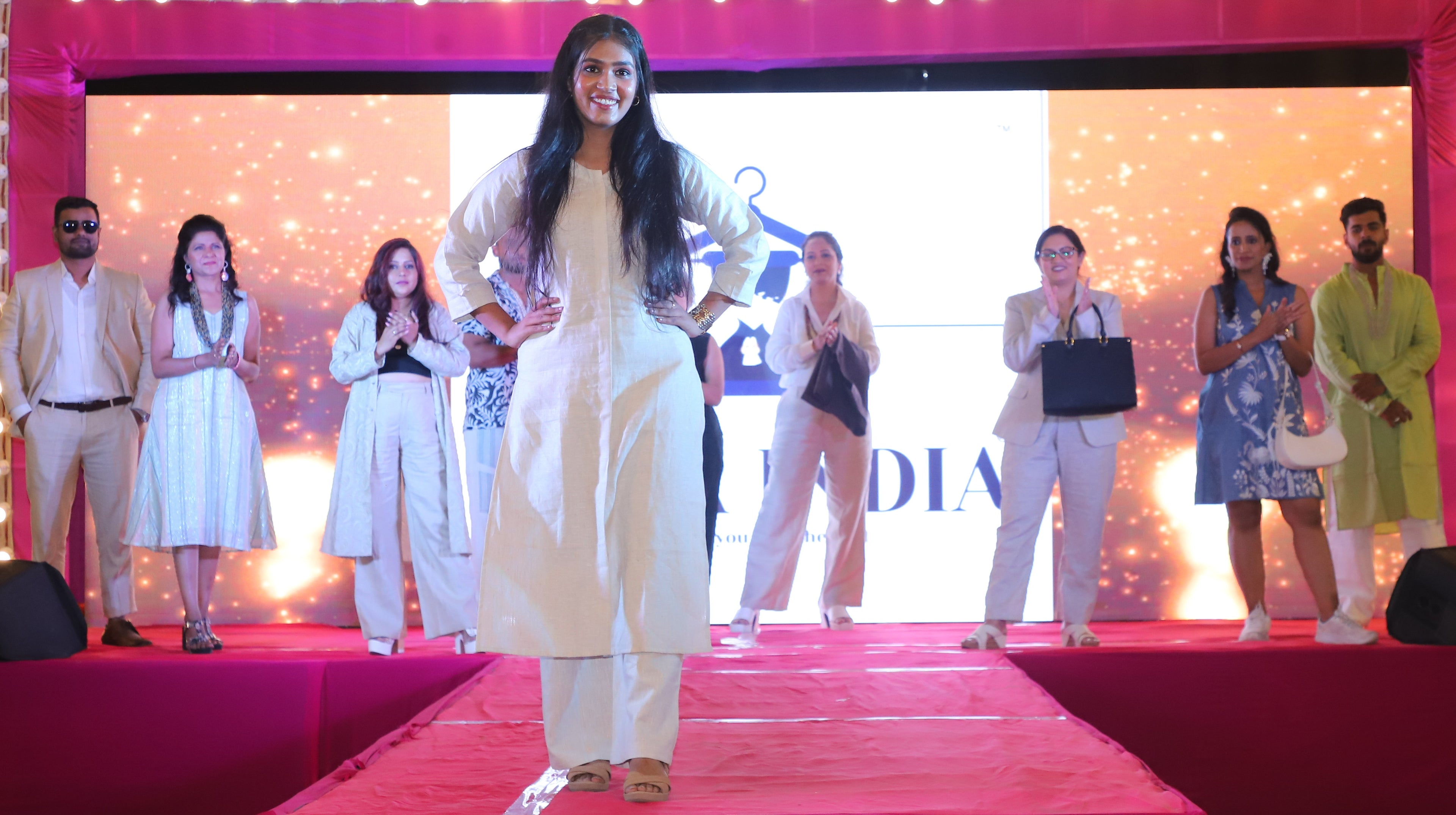 A Woman in a white pure linen outfit on a stage with other people in the background